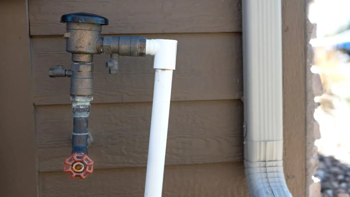 Vacuum breaker valve on a stucco wall beside a downspout, Backflow Prevention in Downey, CA