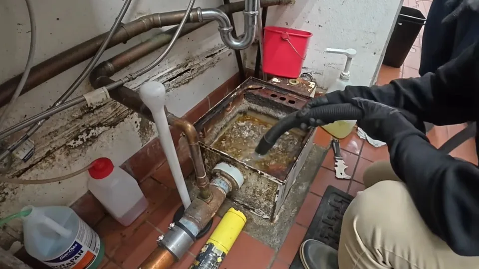 Gloved hand working at a commercial kitchen floor drain and grease line in Downey, CA