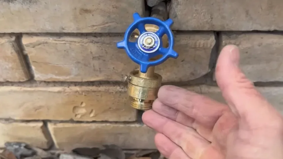 Hand beside an outdoor hose bib with a blue handle on a brick wall, Hose Bib Repair in Downey, CA