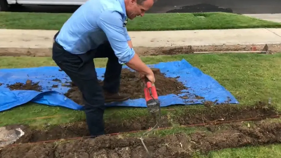 Technician digging a small excavation on a lawn to reach a sewer line in Downey, CA