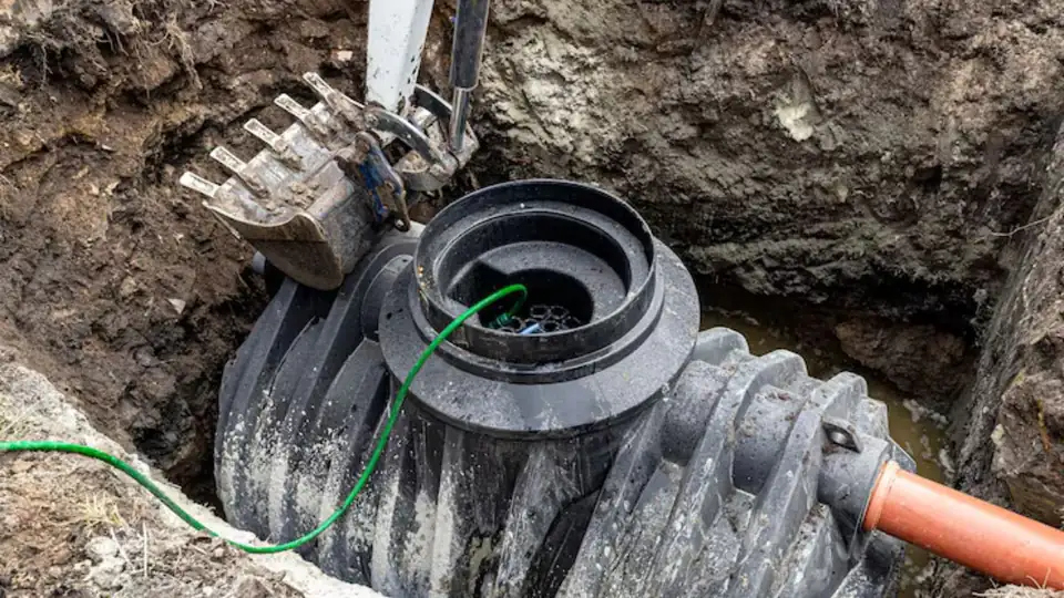 Plastic sump basin with a pump cable and orange discharge pipe set in an excavated pit