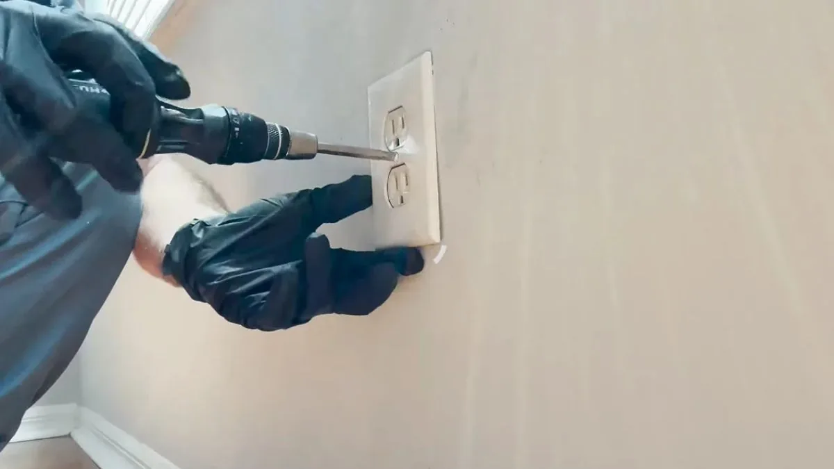 Gloved hand removing an electrical outlet cover on a wet wall during water damage restoration in Downey, CA